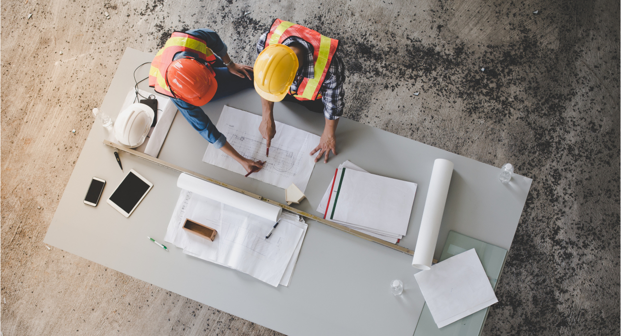 Two construction workers looking over a plan, while discussing how to move forward with their development project.
